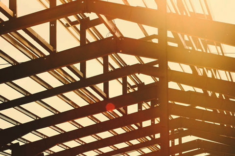 Metal structure being built with sunlight shining through steel rafters