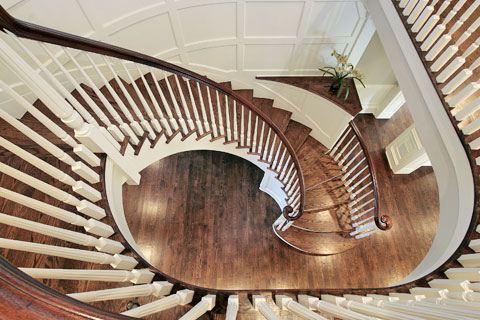 Spiral staircase is framed by dark stained hardwood oak floors and wainscoted walls