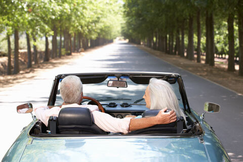 Couple driving down a tree lined street in their classic convertible